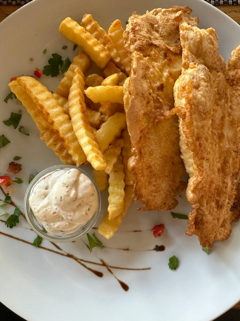pexels-photo-34019400-34019400 Delicious crispy fish with golden crinkle-cut fries and a side of tartar sauce on a white plate.